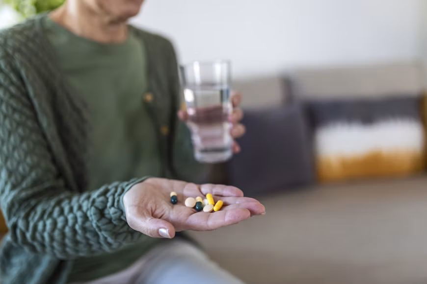 Adult holding medication in one hand and a glass of water in the other.
